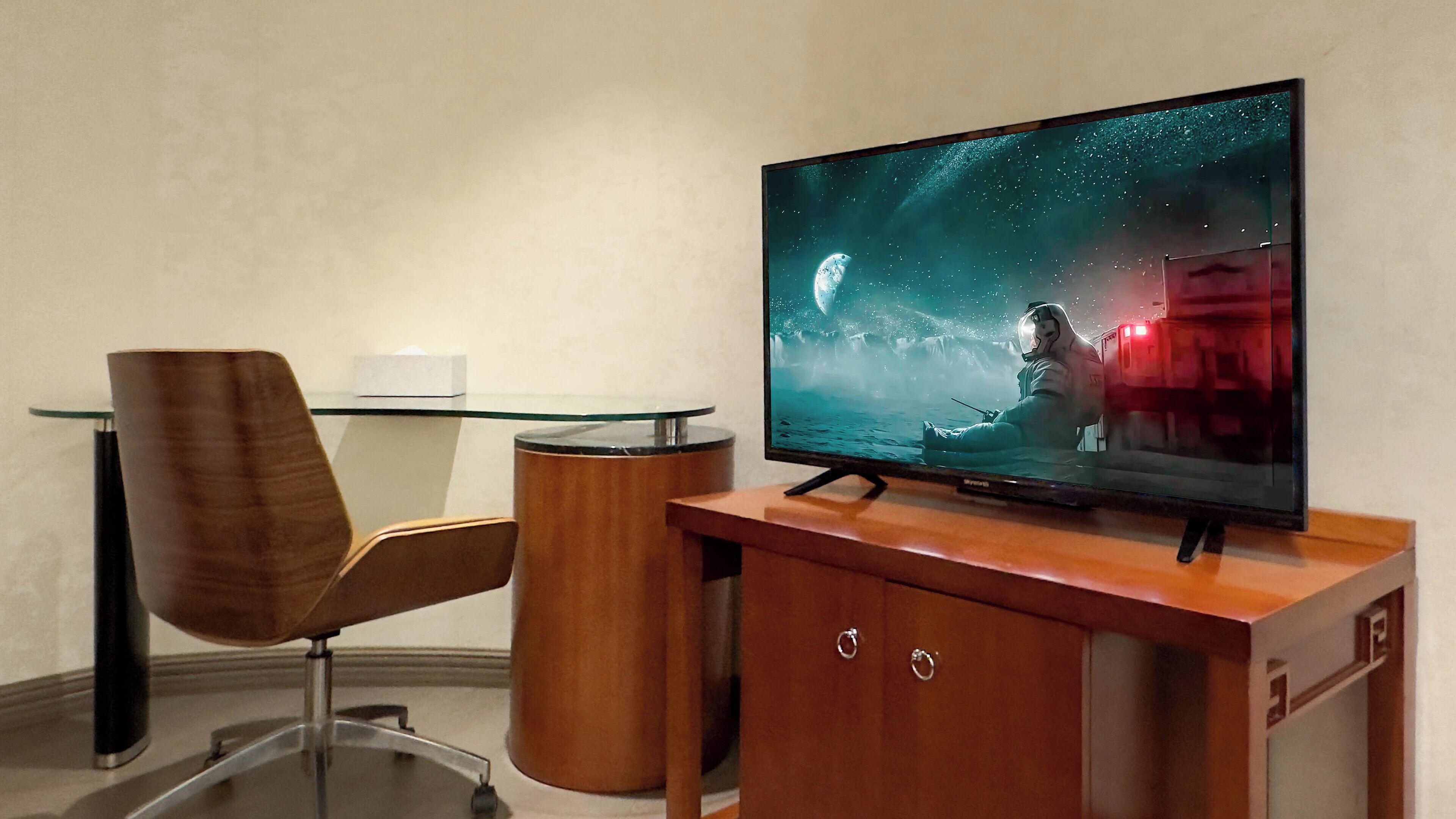 A modern office space with a glass desk, a brown chair, and a television displaying a space-themed scene.