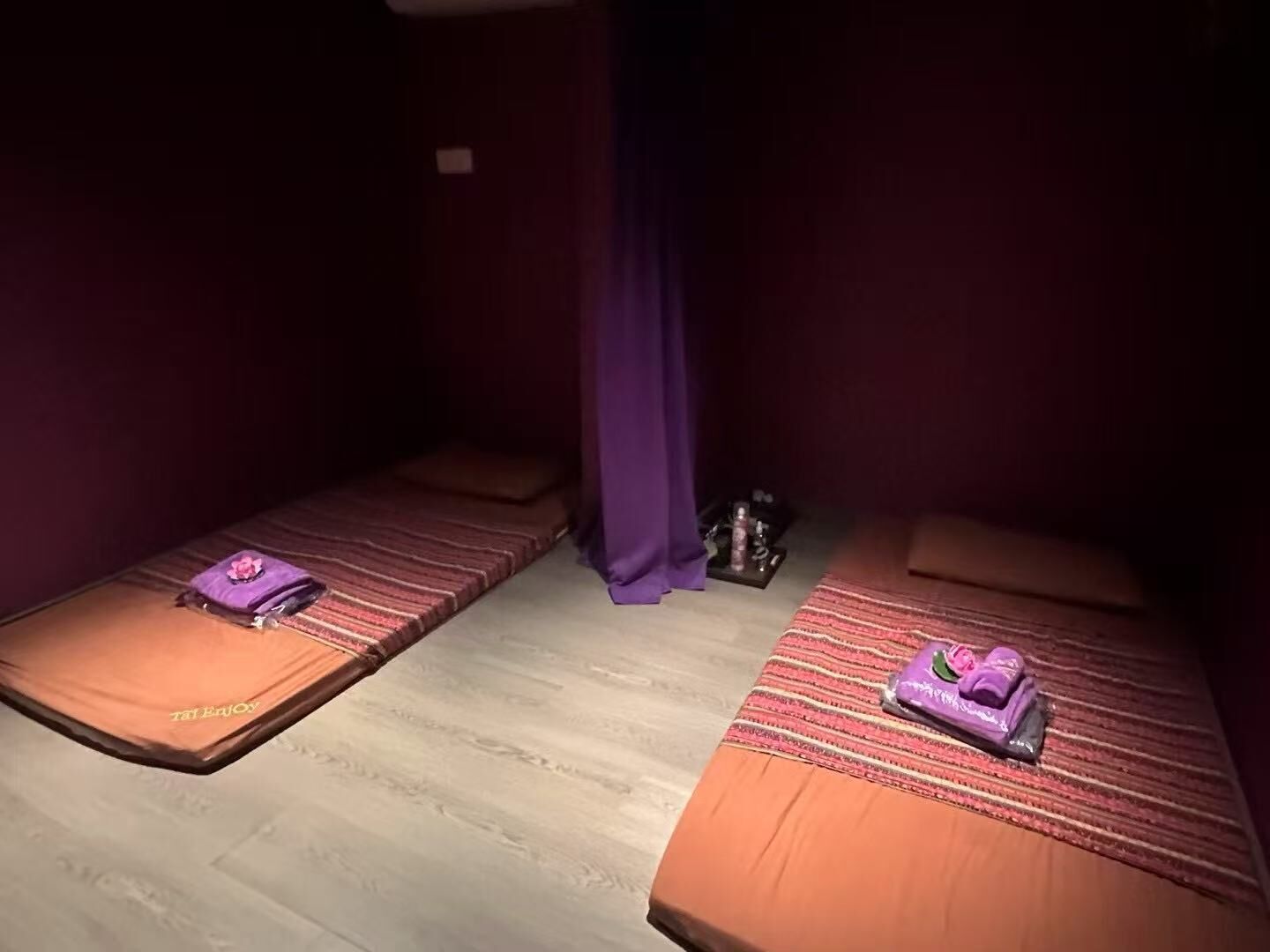 Deux lits simples avec du linge de lit à rayures, une serviette violette et une petite table sur laquelle se trouvent une bouteille et un verre.