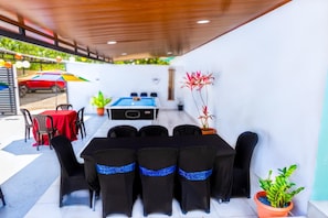 A covered outdoor area with a pool table, chairs, and potted plants.