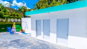 A building with a white exterior and a blue roof, featuring three white doors and a small window. - Villa Stephanie Your Perfect Getaway With Free Pool Table (La Vega)