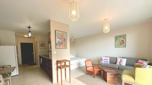 A living room with a sofa, a wooden coffee table, and a dining area with a table and chairs. There are two hanging light fixtures and artwork on the walls. - Fare Hinaiti - Premium Private Studio with sea vue and terrace (Faaa)