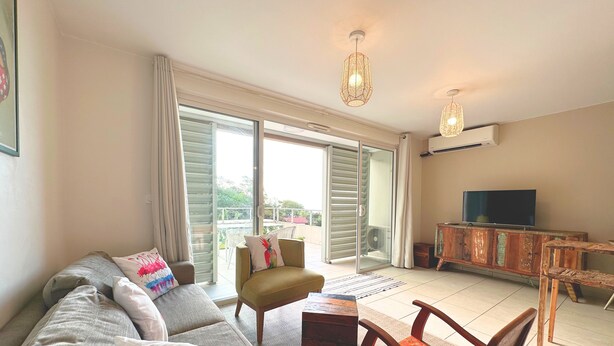 A living room with a sofa, a small table, a TV, and a cabinet. There is a sliding glass door leading to an outdoor area. - Fare Hinaiti - Premium Private Studio with sea vue and terrace (Faaa)