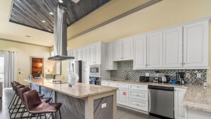 A modern kitchen with white cabinets, a granite countertop, and a central island with bar stools. - Liberty Bluff Dream | 5 bed, 5 bath | Private Pool | Golf Course Views (Kissimmee)