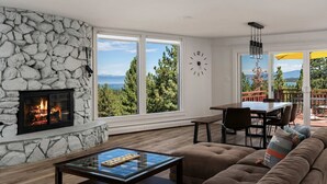 Ein Wohnzimmer mit Kamin aus Stein, großen Fenstern, einem Essbereich und Blick ins Freie.