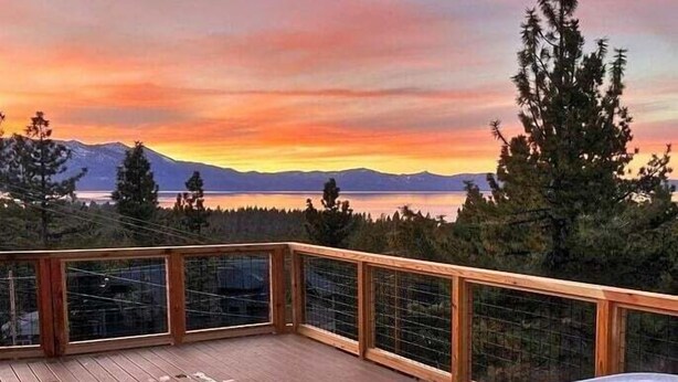 Eine Holzterrasse mit Whirlpool, mit Blick auf einen See und Berge im Hintergrund.
