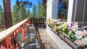 A wooden deck with outdoor furniture, a window with a flower box, and a view of trees.