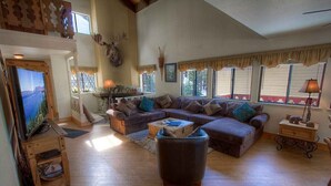 A spacious living room with a sectional sofa, a coffee table, and a television on a wooden stand.
