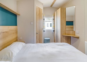A bedroom with a bed, a wooden headboard, a mirror, and a door leading to a bathroom. - 2 Bedroom platinum unit with decking. (Longridge, Ribble Valley)