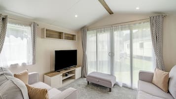 A living room with a flat-screen TV, two sofas, a bench, and large windows with curtains.