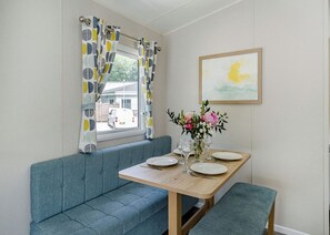 Un comedor con una mesa de madera, un banco azul y una ventana con cortinas estampadas.