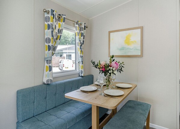 A dining area with a wooden table, blue bench, and a window with patterned curtains.