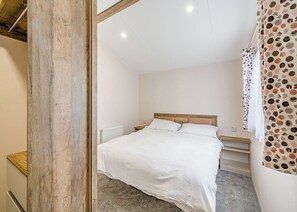 A bedroom with a wooden headboard, a white bedspread, a radiator, and a curtain with a polka dot pattern. - 2 Bedroom platinum unit with decking. (Longridge, Ribble Valley)