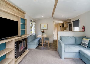 A modern living room with a flat-screen TV, a built-in fireplace, a sofa, a dining table, and a kitchen area. - 2 Bedroom platinum unit with decking. (Longridge, Ribble Valley)