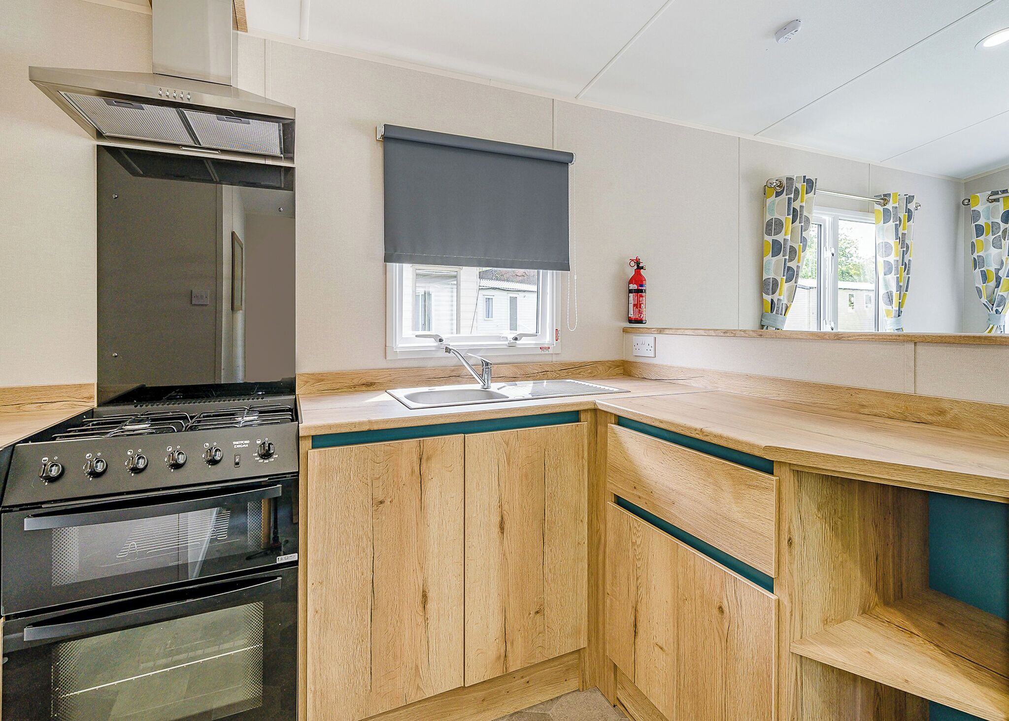 Cocina compacta con estufa a gas, horno y una ventana con persiana enrollable negra.