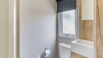 A small bathroom with a toilet, a radiator, a window with a blind, and a sink.