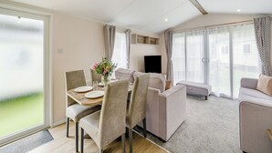 A modern living room with a dining area, a flat-screen TV, and large windows.