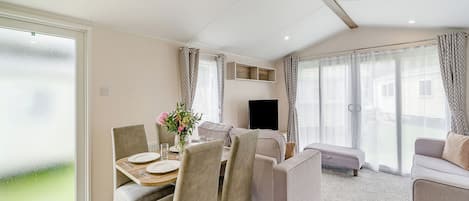A modern living room with a dining area, a flat-screen TV, and large windows.