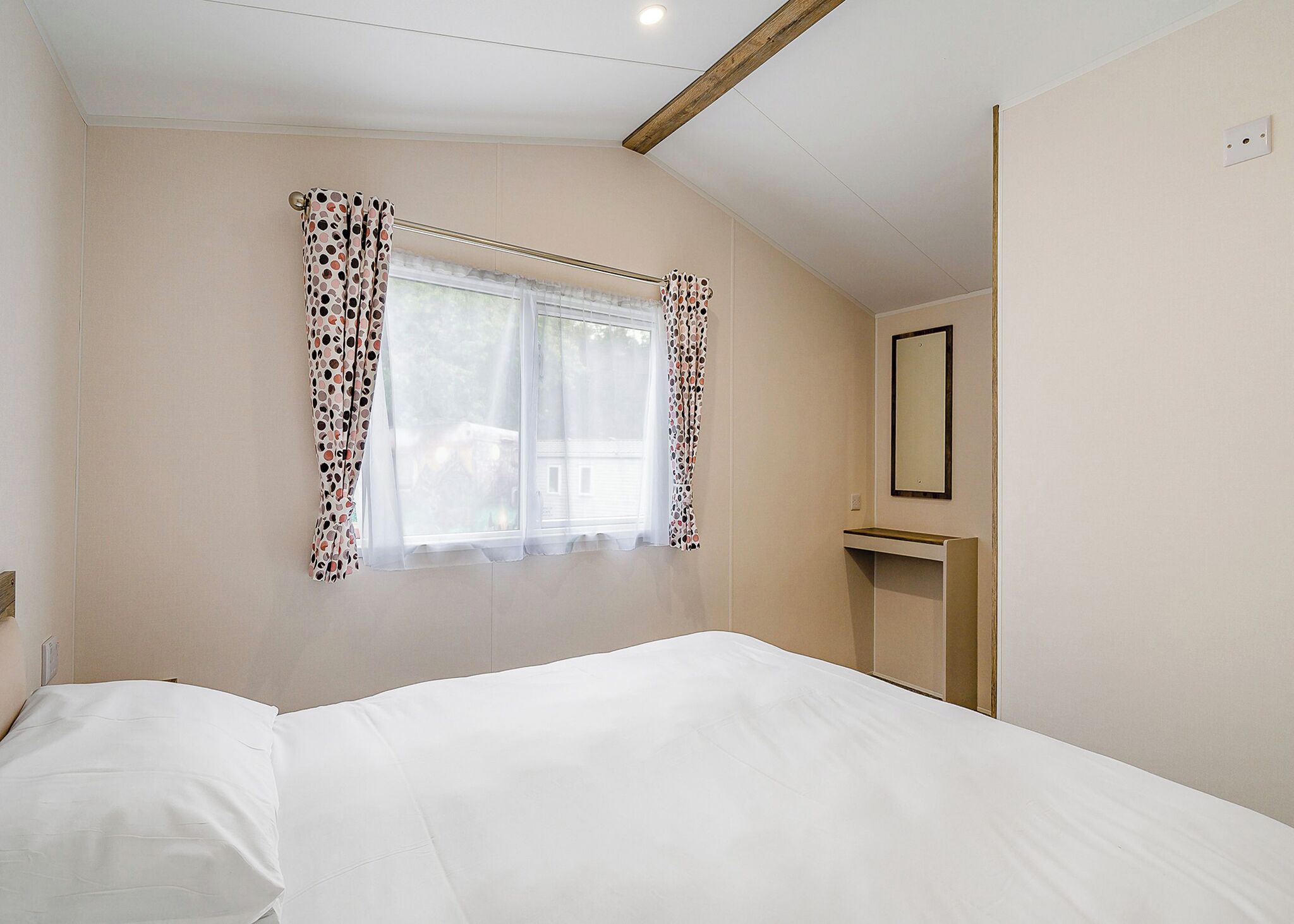 Une chambre à coucher avec un lit, une fenêtre avec des rideaux, un miroir et un plafond avec une poutre en bois.