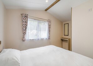 Un dormitorio con cama, una ventana con cortinas, un espejo y techo con vigas de madera.