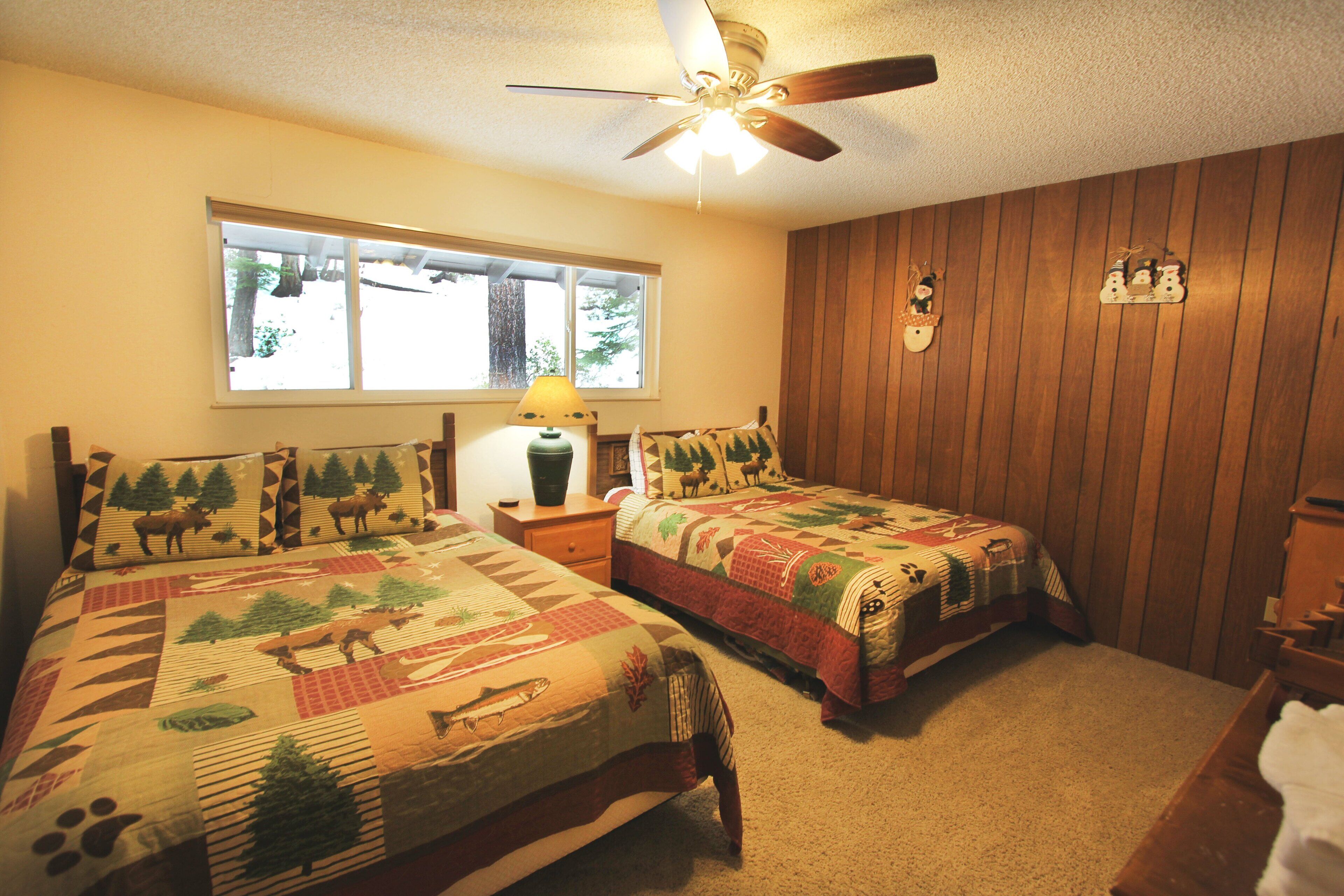 A bedroom with two beds, a ceiling fan, a window, and a wooden wall.