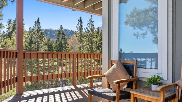 Une terrasse en bois avec une chaise en bois et une petite table agrémentée d’une plante, donnant sur une zone boisée.