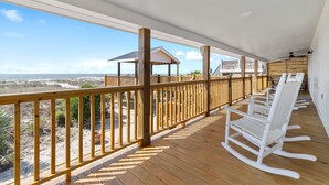 A wooden deck with white rocking chairs, a covered area with a roof, and a view of the beach. - "You are My Sunshine" Fully Renovated, 3 Bedroom, 2 Bathroom, Oceanfront Home (Holden Beach)