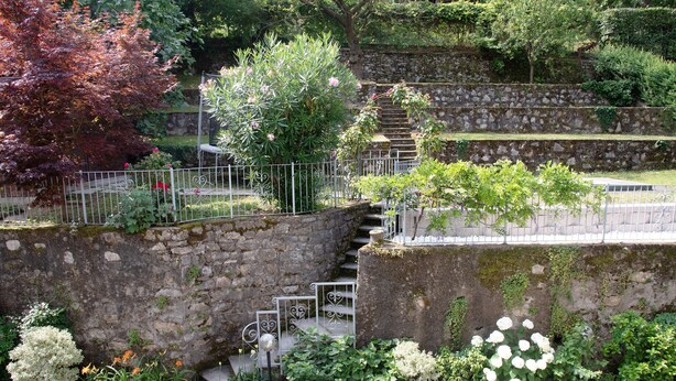 A stone staircase with metal railings, surrounded by lush greenery and flowering plants. - Room 'Stanza 2' with Shared Garden, Wi-Fi and Air Conditioning (Viggiù)