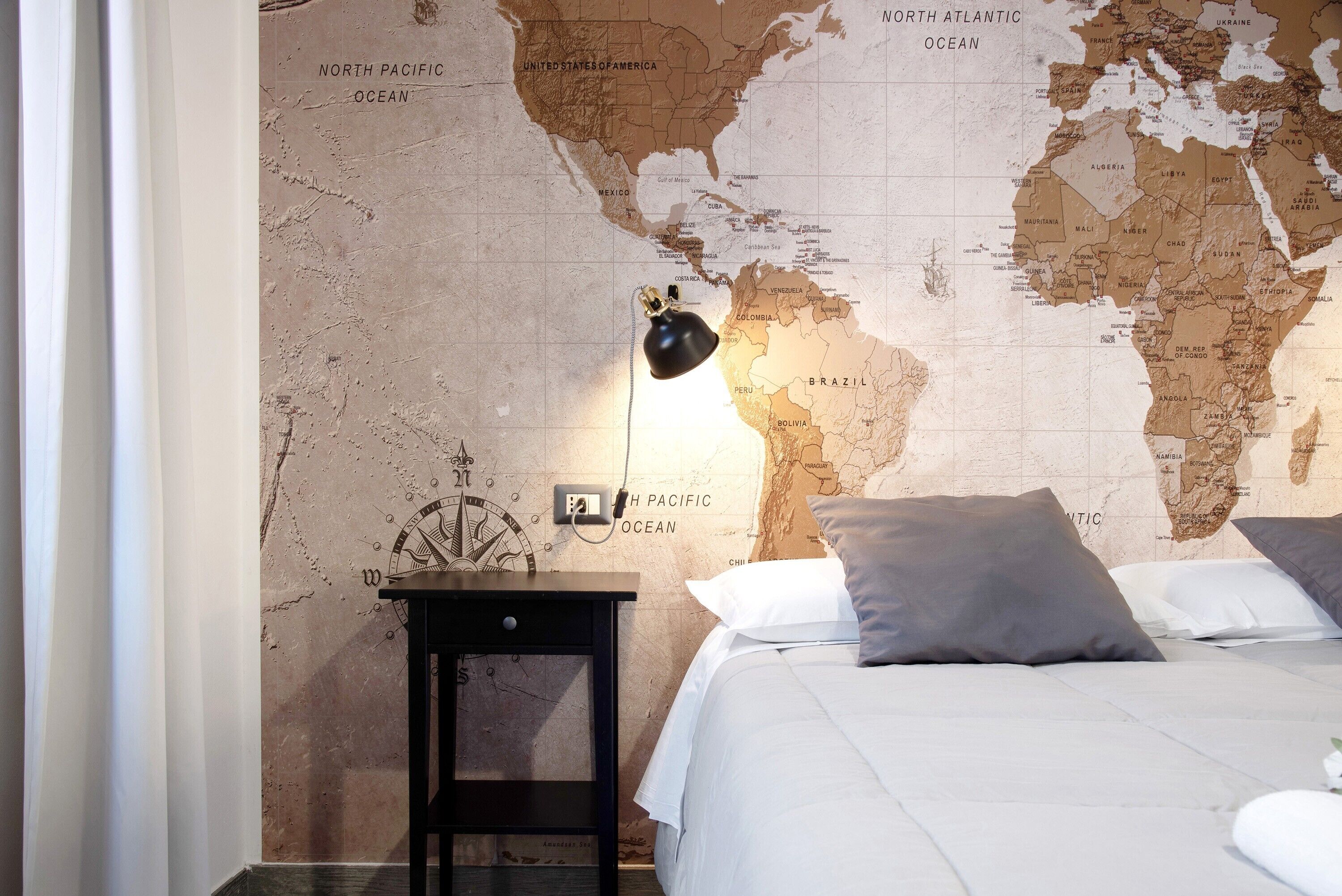 A bedroom with a world map wall, a bed with pillows, a nightstand, and a lamp.