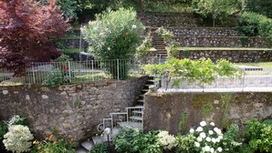 A stone staircase with metal railings, surrounded by lush greenery and flowering plants.