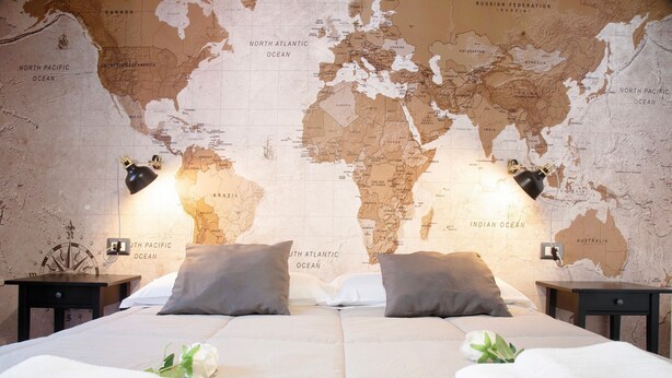 A double bed with two pillows, a world map on the wall, and two bedside lamps.