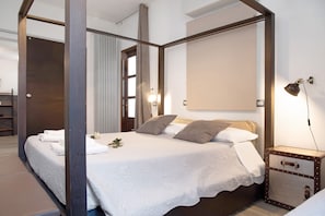 A modern hotel room with a four-poster bed, a bedside table with a lamp, and a large window.