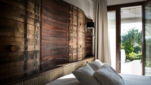 A bedroom with a large wooden headboard, a bed with white linens, and a view of greenery outside. - Room 'Riofavara Winery - Suite Barrique' with Private Terrace, Wi-Fi and Air Conditioning (Ispica)