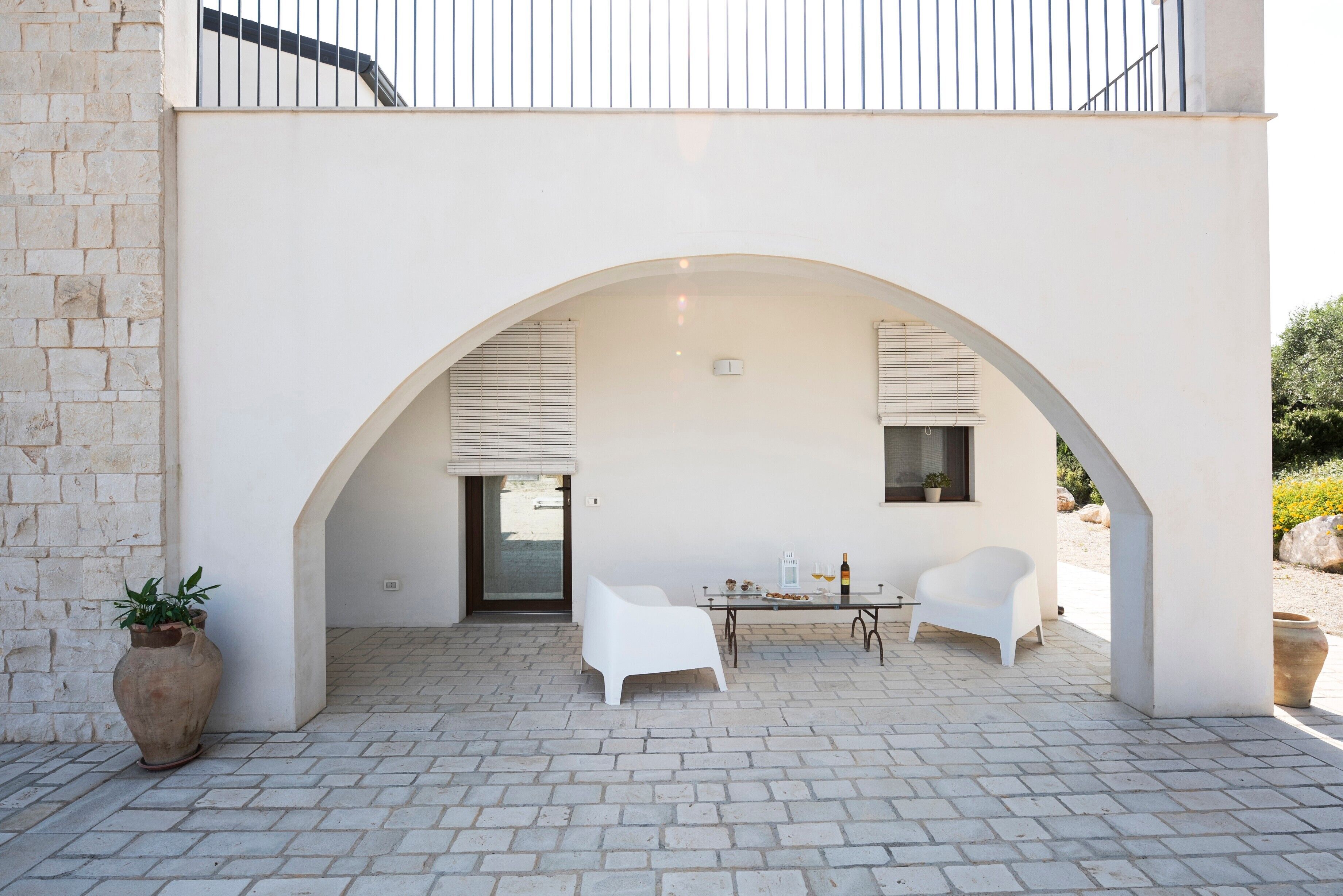 A modern outdoor patio with two white chairs, a table with a bottle, and a potted plant.
