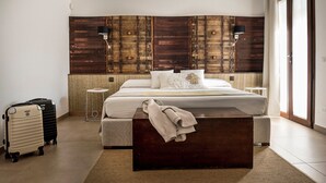 A bedroom with a bed, a wooden headboard, a bedside table, a suitcase, and a window. - Room 'Riofavara Winery - Suite Barrique' with Private Terrace, Wi-Fi and Air Conditioning (Ispica)