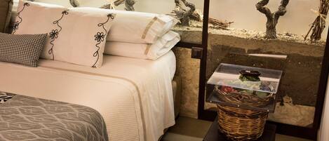 A neatly made bed with white linens and decorative pillows, a wicker basket on a small table, and a wall with a decorative tree design.