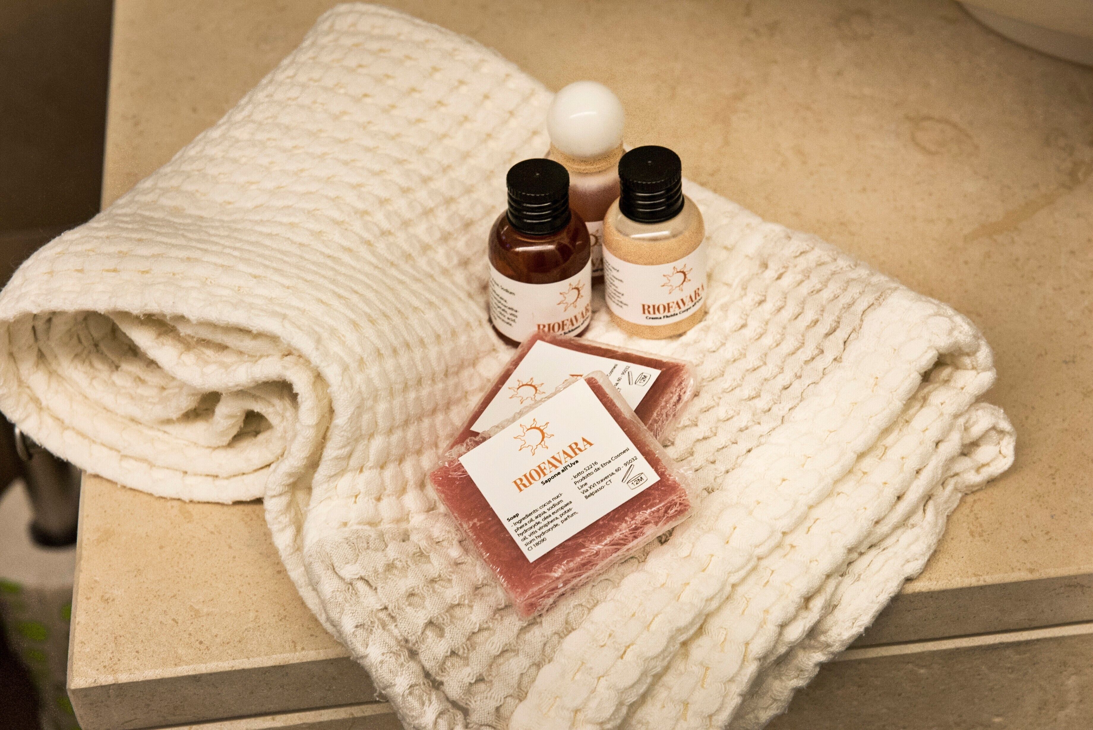 A textured white towel, two bottles of liquid soap, and a bar of soap on a beige surface.