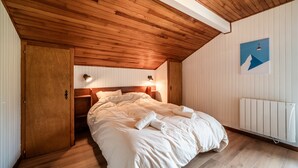 Ein Schlafzimmer mit Holzboden, einem Bett mit weißer Bettwäsche, einem an der Wand montierten Heizkörper und einem Bild von einem Berg.