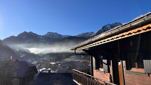Ein Bergdorf mit traditionellen Holzhäusern, blauem Himmel und schneebedeckten Gipfeln im Hintergrund.
