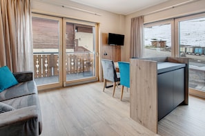 Una habitación de hotel moderna con sofá, sillas, televisión y ventanas amplias que dan a un paisaje nevado.