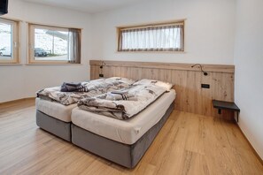A bedroom with a bed, two windows, a wooden headboard, and a small shelf.