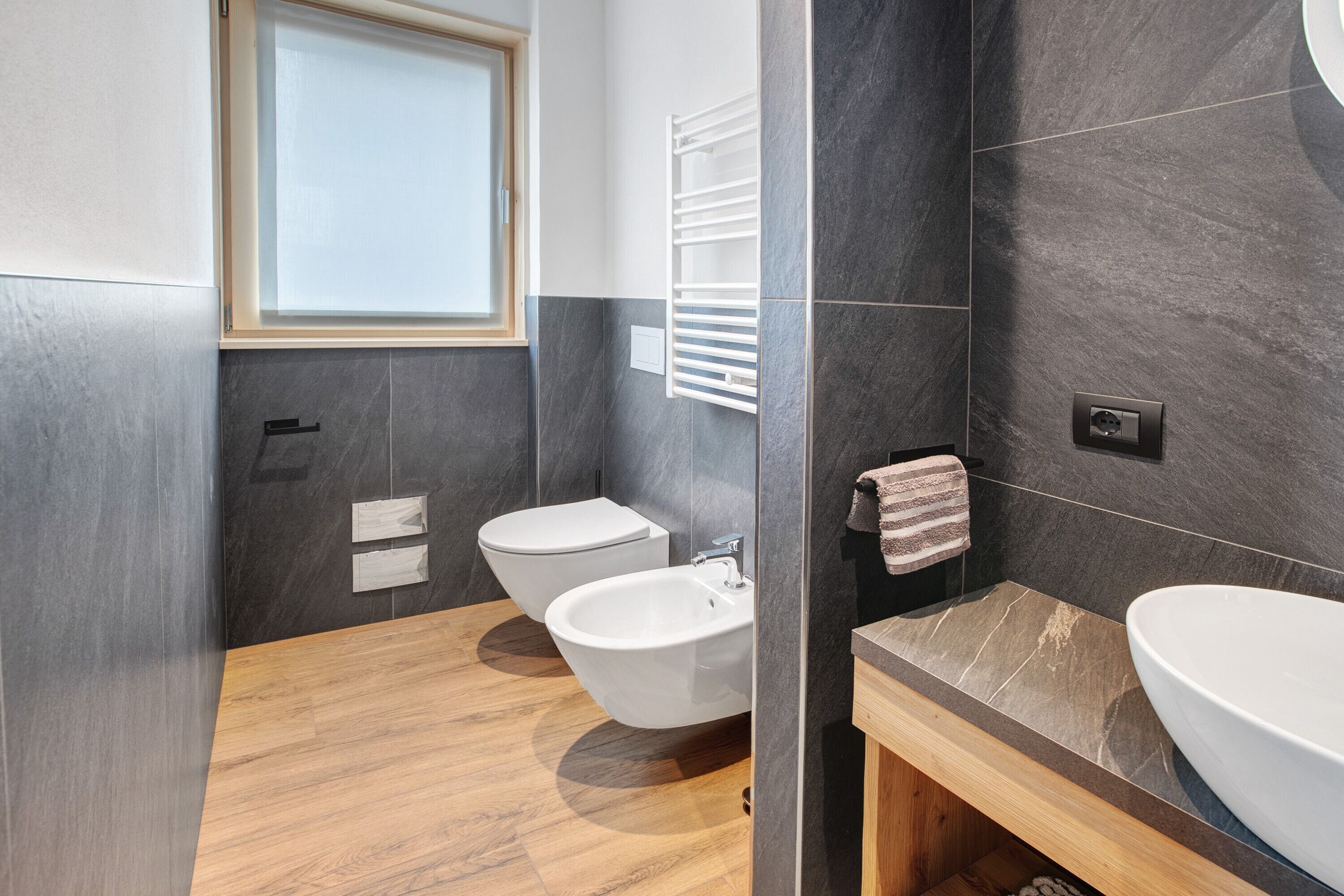 A modern bathroom with a bidet, a sink, a towel rack, and a window.
