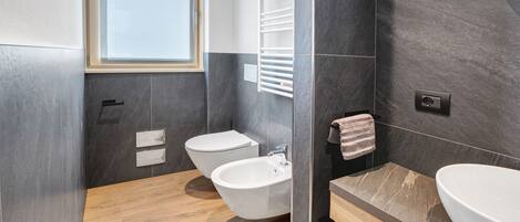 A modern bathroom with a bidet, a sink, a towel rack, and a window.