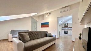 Un soggiorno moderno con un divano, una TV e una cucina sullo sfondo.