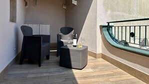 Un balcone con mobili in vimini, un tavolino con una bottiglia e un bicchiere, e una bicicletta sullo sfondo.