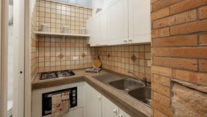 Una cocina funcional con estufa a gas, lavamanos y alacenas blancas.