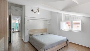 Quarto com cama, soalho de madeira, luminária no teto e janela.