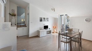 A modern kitchen with a dining area, white cabinetry, a flat-screen TV, and a vase with flowers. - Apartment 'Tramonto' with Mountain View, Wi-Fi and Air Conditioning (Pimonte)