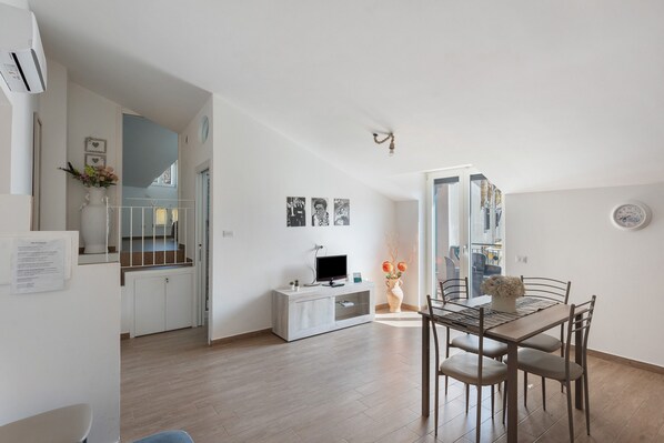 Una cocina moderna con comedor, muebles blancos, un televisor de pantalla plana y un florero con flores.