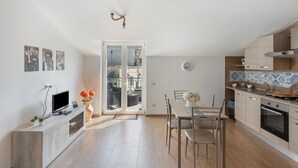 A modern kitchen with a dining area, a TV on a wooden console, and a view through the glass door. - Apartment 'Tramonto' with Mountain View, Wi-Fi and Air Conditioning (Pimonte)