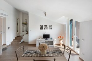 Una sala de estar moderna con comedor, una escalera y un televisor sobre un mueble blanco.